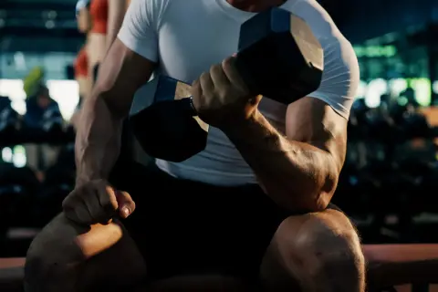 Mężczyzna ćwiczy biceps na wyciągu, napinając mięśnie podczas podnoszenia ciężaru.