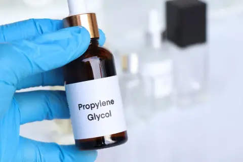 Ręka w niebieskiej rękawiczce trzyma buteleczkę z etykietą "Propylene Glycol".