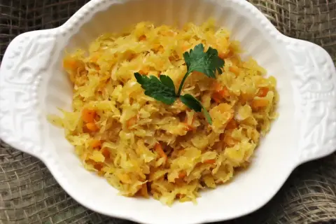 Pyszna kapusta kiszona gotowana z marchewką, udekorowana natką pietruszki, podana w białej miseczce.