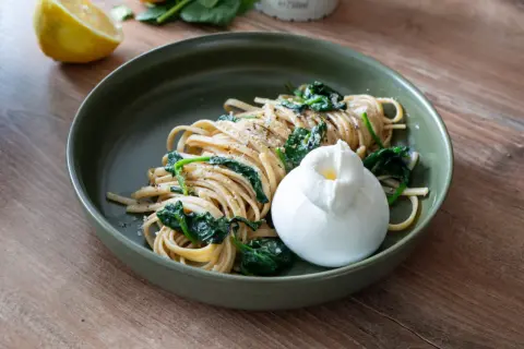 Zitronen Pasta mit Spinat und Burrata auf einem grünen Teller, daneben eine Zitronenhälfte.