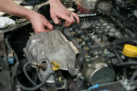 Mechanik pracuje przy silniku, diagnozując objawy uszkodzonego czujnika położenia wałka rozrządu.