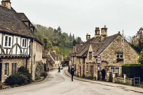 Kamienna uliczka w Cotswolds, z tradycyjnymi domami i drzewami na wzgórzach.