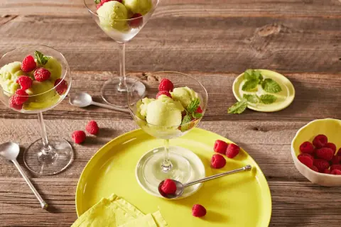 Erfrischendes Kiwi-Sorbet mit Himbeeren und Minze in eleganten Gläsern auf Holzhintergrund.
