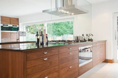 Cuisine moderne avec îlot central en bois, hotte en inox et vue sur jardin. Une belle rénovation pour une vieille cuisine.