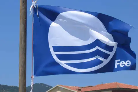 Bandiera blu con logo FEE sventola su un cielo azzurro, simbolo di qualità ambientale.