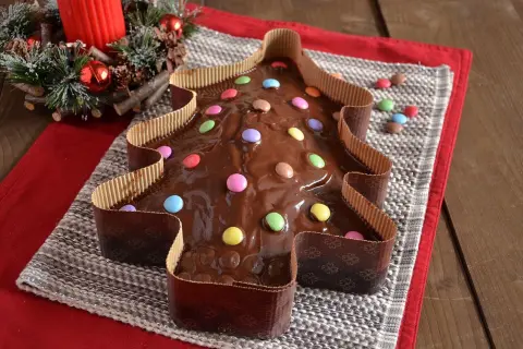Dolce a forma di albero di Natale ricoperto di glassa al cioccolato e decorato con caramelle colorate.