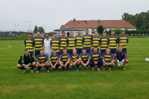 Drużyna KS Iskra Stolec gotowa do meczu. Piłkarze w żółto-niebieskich strojach, jeden w bramkarskim.
