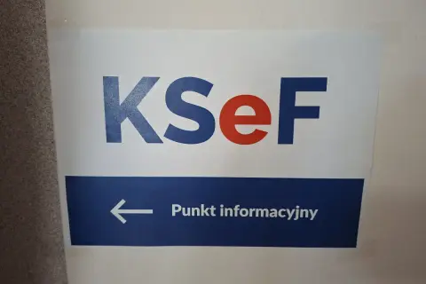 Tablica informacyjna KSeF. Strzałka w lewo wskazuje punkt informacyjny, gdzie można uzyskać pomoc podczas szkolenia.
