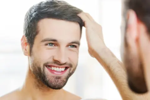Hombre sonriente se toca el cabello, reflejando su confianza en sus tratamientos de belleza para hombres.