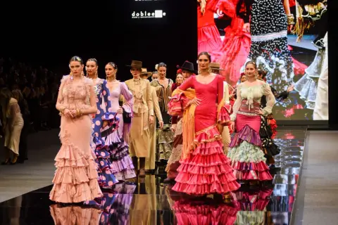 Modelos desfilan en la **pasarela SIMOF** con trajes de flamenca vibrantes y volantes.