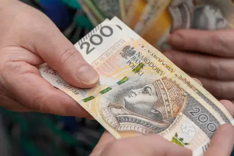 Dwie dłonie przekazują sobie banknot 200 zł. Czy wychowanie dzieci liczy się do emerytury?