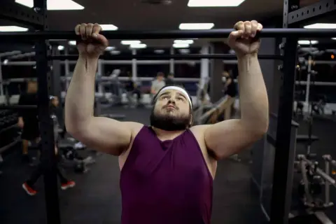 Uomo con fisico endomorfo si allena in palestra, concentrato su una trazione alla sbarra.