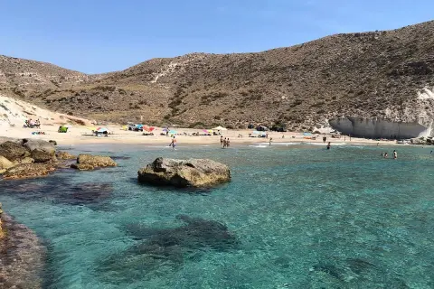 Aguas cristalinas en la cala del medio, con gente disfrutando del sol y el mar en un día soleado.