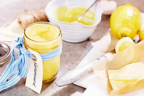 En burk med krämig lemon curd, redo för ett recept. Citroner och smör ligger bredvid.