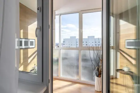 Zabudowany balkon z widokiem na budynki, ozdobiony wazonem z gałązkami.