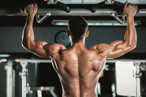 Mężczyzna wykonuje podciąganie na drążku, napinając potężne **biceps**y.