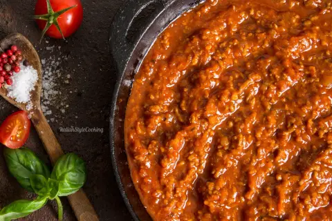 Herzhafte Bolognese-Sauce in einer Pfanne, mit frischen Tomaten, Basilikum, Salz und Pfefferkörnern als Zutaten für Bolognese.