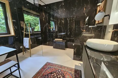 Luxuriöses Bad ohne Fenster mit schwarzem Marmor, freistehender Badewanne, Dusche und Waschbecken. Ein bunter Teppich liegt auf dem Boden.