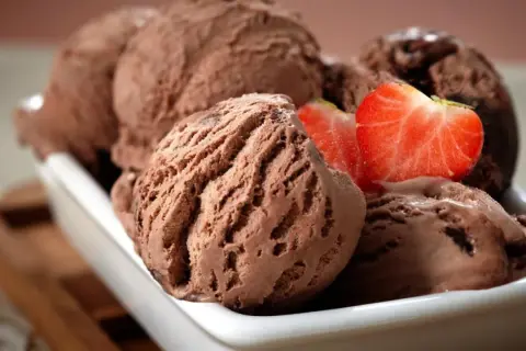 Cremoso helado de chocolate servido en un cuenco blanco, decorado con fresas frescas.