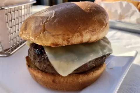 Hamburger z serem na białym talerzu, obok koszyka na frytki.