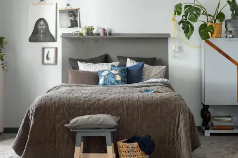Ett mysigt grått rum med en stor säng, konst på väggen och en grön växt.