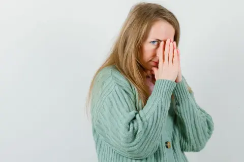 Een vrouw met blond haar, die haar gezicht bedekt met haar handen, lijkt overprikkeld, wat kan duiden op hsp en trauma.