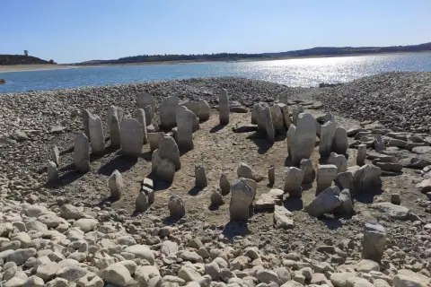 El dolmen de Guadalperal emerge de las aguas bajas, un círculo de piedras ancestrales bajo un cielo azul.