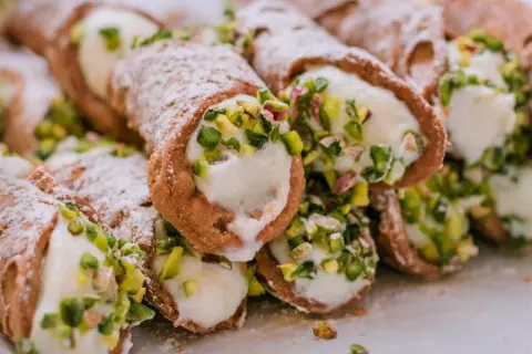 Stos delikatnych, włoskich rurek z kremem i pistacjami, posypanych cukrem pudrem.