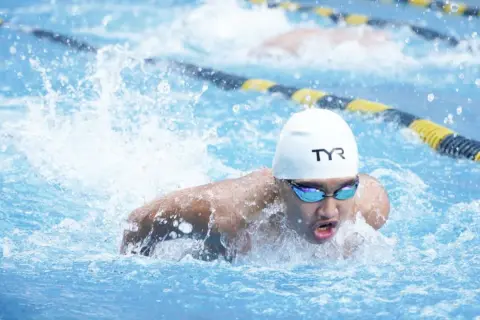 A swimmer in a white cap and goggles powers through the water, demonstrating technique for how to swim faster.