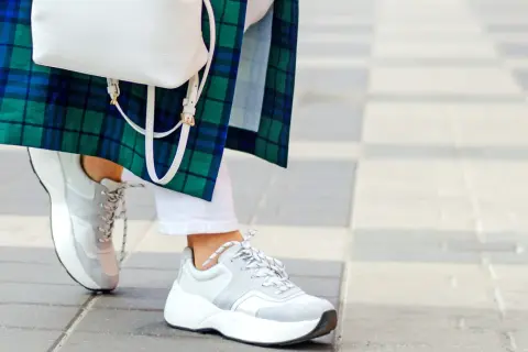 Stylowe białe sneakersy damskie idealnie komponują się z białą stylizacją i zielono-niebieską kraciastą marynarką.