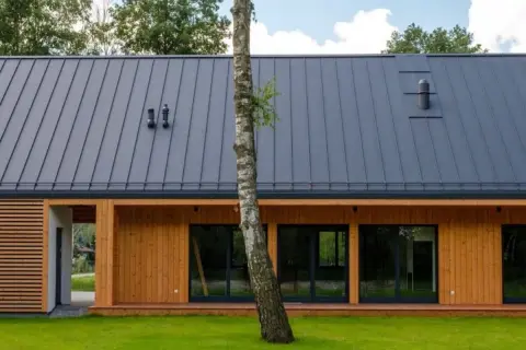 Nowoczesny dom szkieletowy bez pozwolenia, z drewnianą elewacją i szarym dachem, otoczony zielenią.