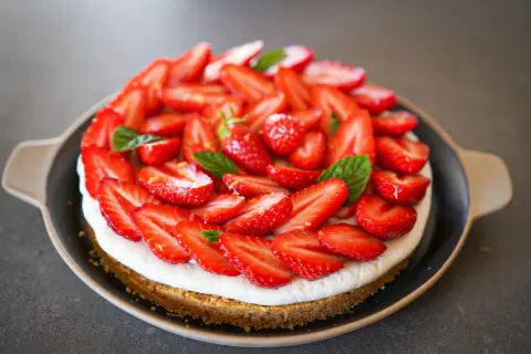 Tarte aux fraises mascarpone, une gourmandise estivale recouverte de fruits rouges frais et de feuilles de menthe.