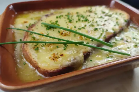 Zuppa di cipolle fumante, con crostini dorati e formaggio filante, guarnita con erba cipollina fresca.