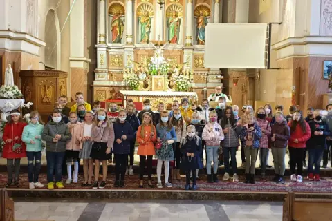 Dzieci w kościele, każde z różańcem w ręku, zastanawiają się, czy można samemu poświęcić różaniec.