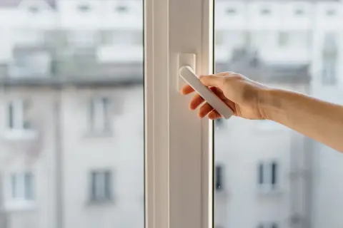 Mano girando la manija de una ventana osciloparalela, quizás para solucionar problemas de apertura o cierre.