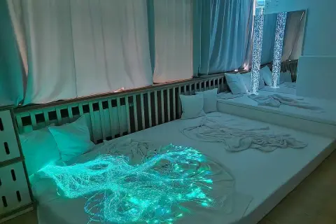 Ein beruhigender Snoezelen Raum mit weißen Matratzen, Kissen und faszinierenden Lichteffekten, darunter leuchtende Glasfasern.