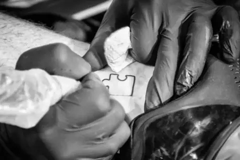 Ręce w rękawiczkach tworzą tatuaż puzzle, symbol autyzmu.