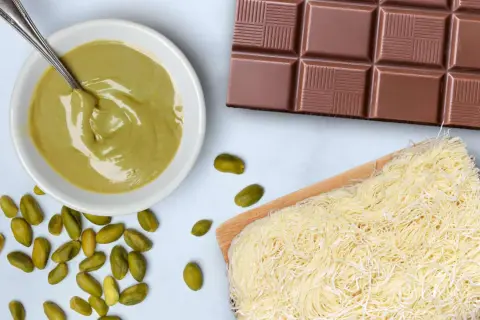 Zutaten für ein **Rezept Dubai Schokolade**: Pistaziencreme, Schokoriegel, Kataifi-Teig und ganze Pistazien.