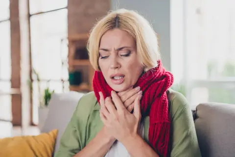 Kobieta z czerwoną szalikiem na szyi, z bólem gardła, może to być objaw dyfterytu.