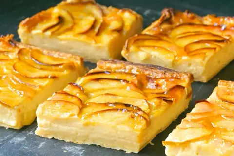 Porciones de tarta de manzana con crema pastelera, cubiertas con glaseado brillante y rodajas de manzana caramelizadas.