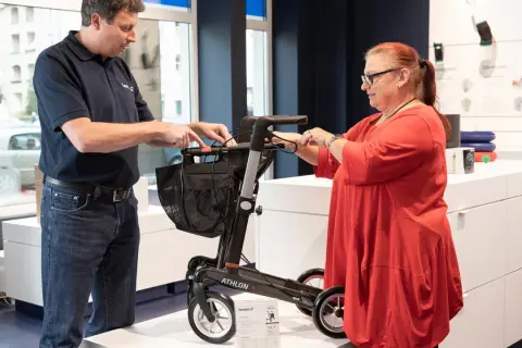 Mann erklärt einer Frau einen Rollator. Eine medizinische Hilfsmittel Liste ist im Hintergrund zu sehen.