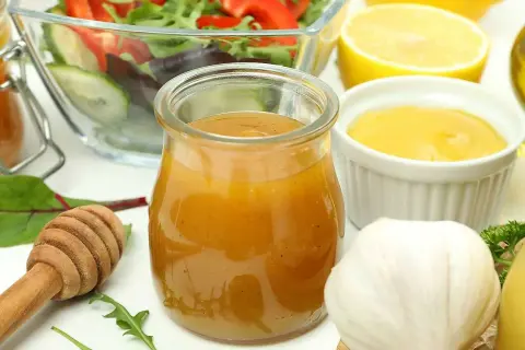 En burk med gyllene salladsdressing, bredvid en skål med sallad, citron, vitlök och honung. Ett perfekt salladsdressing recept!