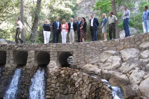 Un grupo de personas celebra en el lugar donde nace el río Andarax, con cascadas cayendo bajo un puente de piedra.