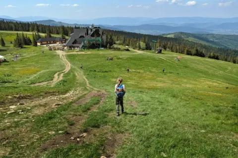Dziecko z plecakiem idzie ścieżką na hali miziowej. W oddali budynki i góry.