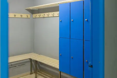 Un vestiaire avec des casiers bleus, des bancs en bois et des patères.