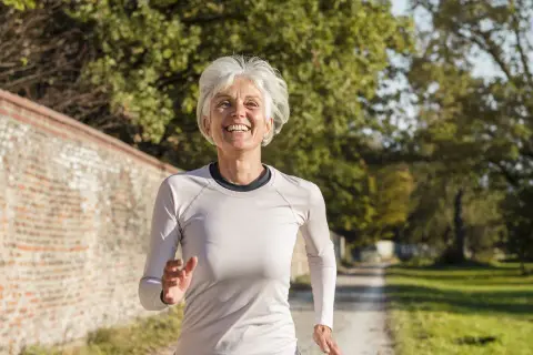 Femme souriante de 60 ans courant sur un chemin, suivant un plan d'entraînement course à pied.