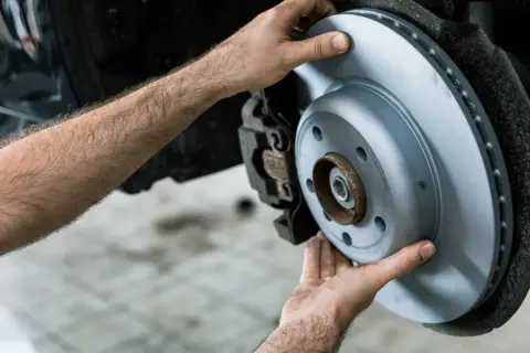Mains d'un mécanicien installant un disque de frein neuf pour éviter le frein qui grince.