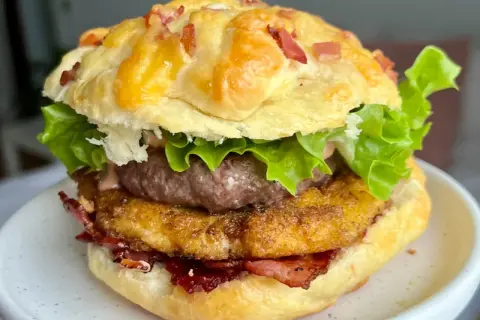 Domowy burger z serem, bekonem, kotletem i sałatą na talerzu.