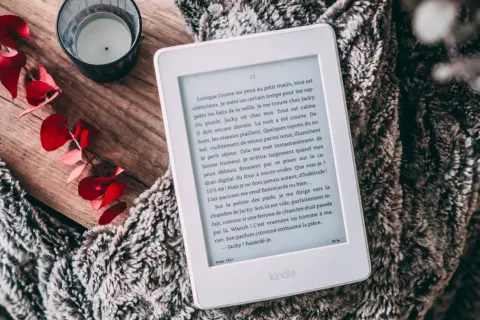 Un ebook Fnac sur Kindle, posé sur une couverture douillette, avec des feuilles rouges et une bougie.