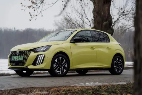 Żółty Peugeot e-208 stoi na tle drzew i zimowego krajobrazu.